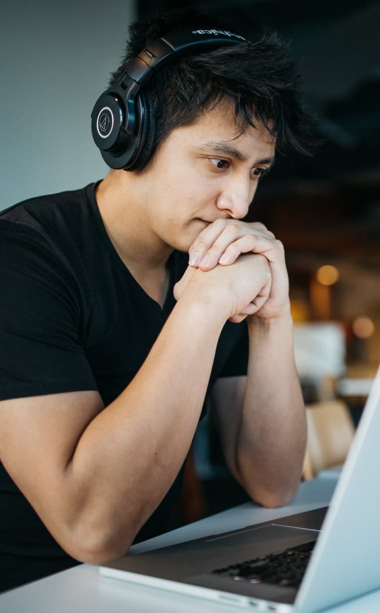 Person deep in thought, wearing headphones, looking at laptop screen